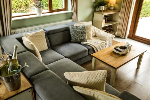 Modern sitting area at Greenvale Cabins in Newry with gray sectional sofa, wooden coffee table, and garden views through