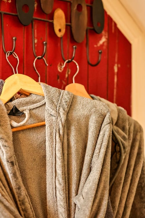 Towels and robes hanging on wooden hangers against red wall in Greenvale Apartment, Newry
