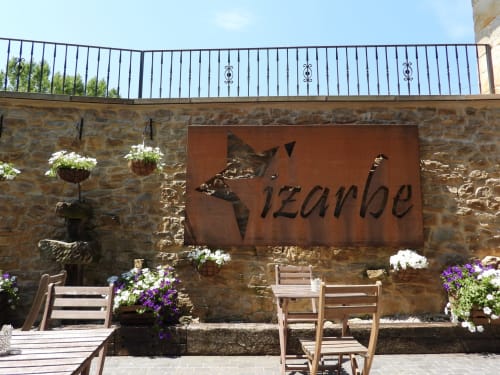 Patio del Hotel Rural Izarbe en Burgos con muros de piedra rústica, mobiliario de madera, plantas floridas y vistas a las montañas