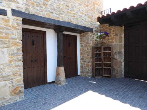 Patio de piedra de la casita rural Hotel Izarbe en Burgos con puertas de madera, vigas oscuras y flores colgantes