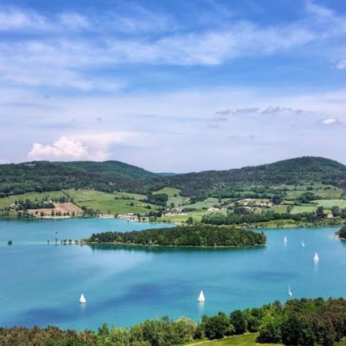 Türkisfarbener See mit Segelbooten, bewaldeter Insel und grünen Hügeln bei Mirepoix, Ariège
