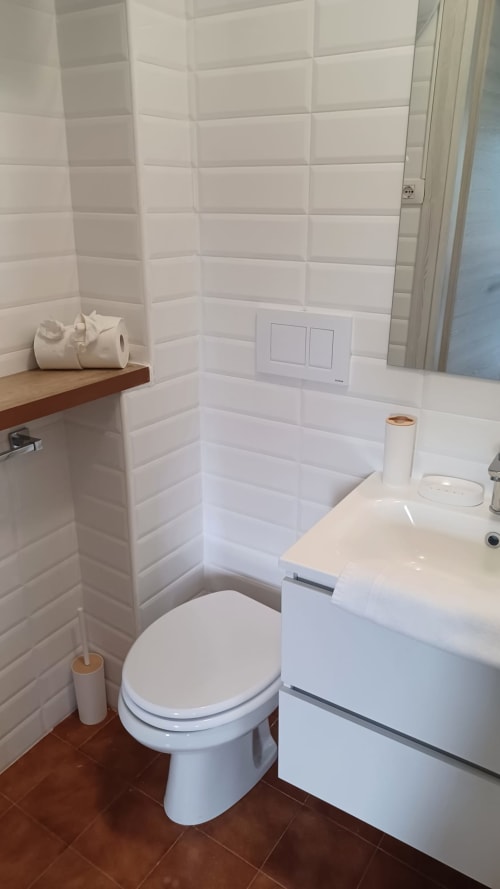 Bagno moderno nella collezione THE V Milano con piastrelle bianche, sanitari, lavabo e accenti in legno