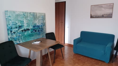 Zona living moderna dell'Appartamento Sormano, THE V Collection Milano, con divano teal, tavolo in legno e opera astratta turchese