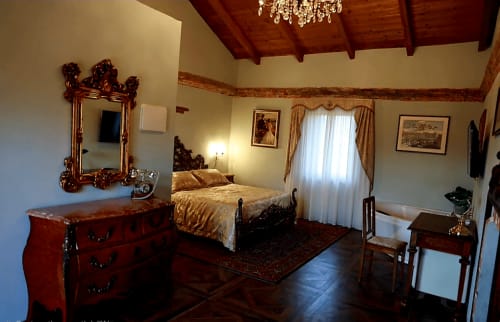 Elegante camera da letto suite nella Cascina Tavella di Rivalta di Torino con travi in legno, specchio ornamentale e vista sulle montagne