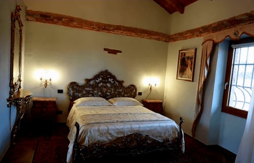 Elegante suite del B&B Cascina Tavella a Rivalta di Torino con letto in legno ornato, pareti color crema, travi a vista e montagne