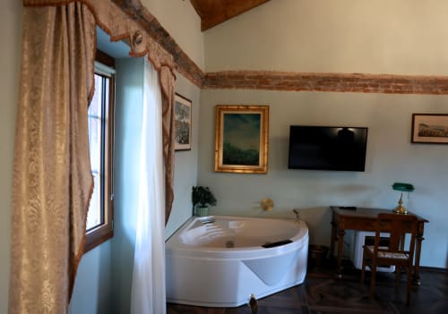Bagno della suite lusso B&B Cascina Tavella con vasca d'angolo bianca, travi in laterizio a vista, TV e vista sulle montagne