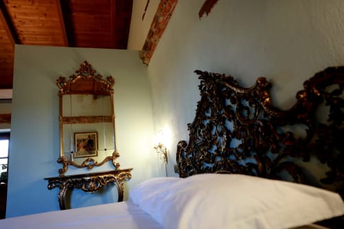 Suite elegante del B&B Cascina Tavella con specchio dorato ornato, testata scura intagliata e biancheria bianca a Rivalta di