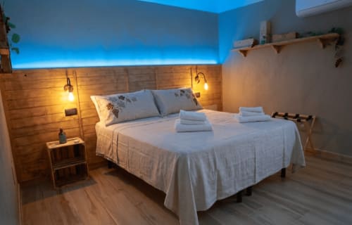 Camera moderna della B&B Cascina Tavella con testata in legno, illuminazione blu e biancheria bianca a Rivalta di Torino