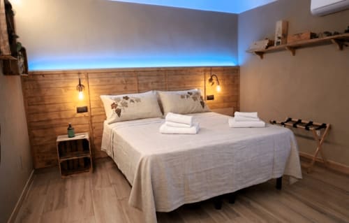 Camera moderna del B&B Cascina Tavella con testata in legno, illuminazione blu, biancheria bianca e arredamento rustico a Rivalta