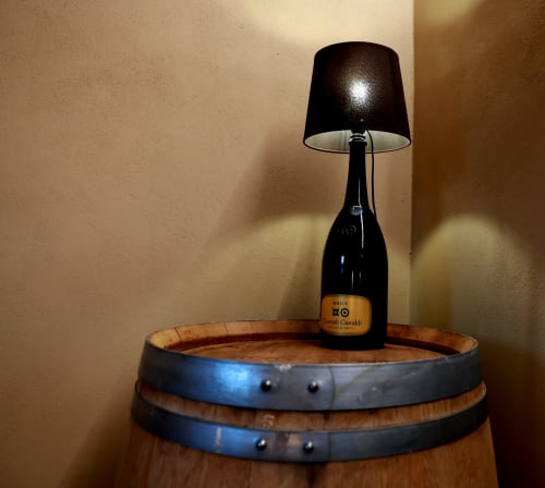 Bottiglia di vino con lampada nera su botte in legno nella Camera delle Botti di B&B Cascina Tavella, Rivalta di Torino