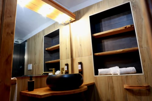 Bagno moderno di B&B Cascina Tavella con lavabo in pietra nera, mobile in legno, specchio, scaffali con asciugamani e illuminazione ambient