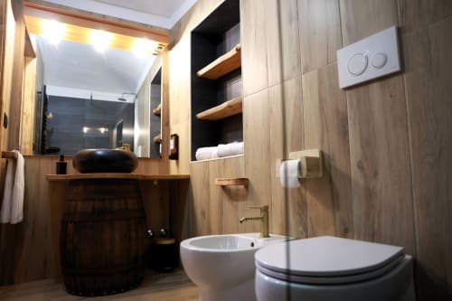 Bagno moderno del B&B Cascina Tavella con lavabo nero, wc bianco, dettagli in legno e specchio illuminato a Rivalta di