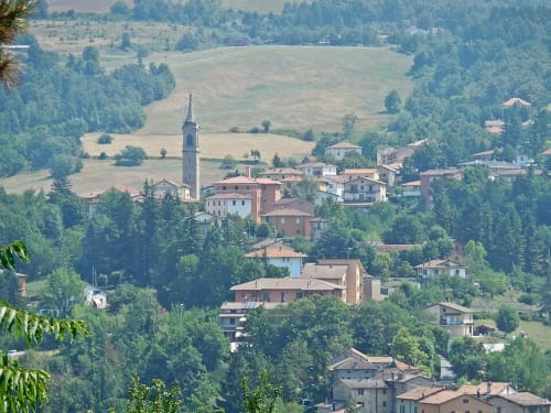 Vista aerea del villaggio di San Benedetto Val di Sambro immerso in dolci colline verdi con campanile e case in pietra sparse