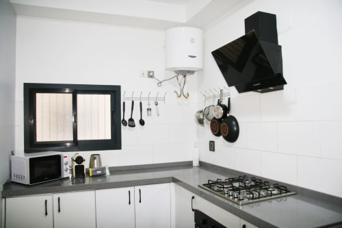 Modern equipped kitchen in Dakar apartment with gas cooktop, black range hood, and organized utensil storage