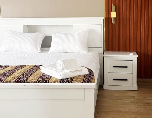 Modern bedroom in Dakar apartment with white bed, striped pillows, patterned throw, and wooden bedside table with gold