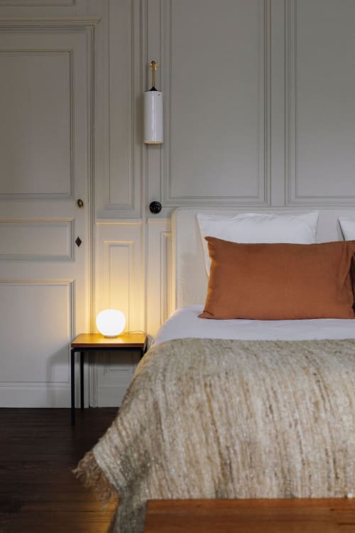 Modern bedroom at Trama en Perche with beige paneled walls, bed with rust pillow, pendant lamp, and glowing nightstand light.
