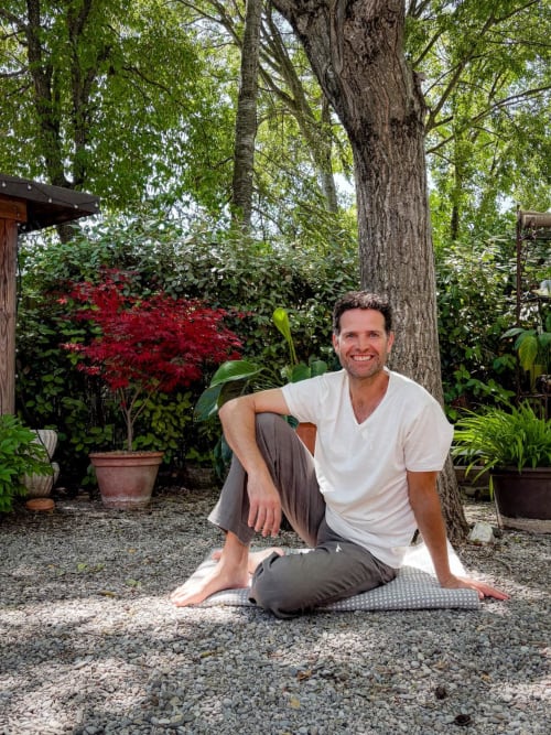 Man smiling in lush garden at Le Bacalan B&B in Mormoiron, France, surrounded by greenery and red foliage