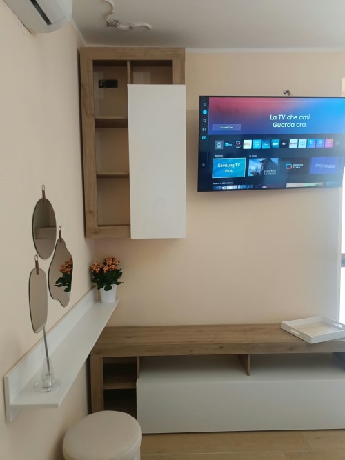 Camera moderna presso Atena Smartrooms a Sellia con TV a parete, mobile in legno, fiori in vaso e design minimalista