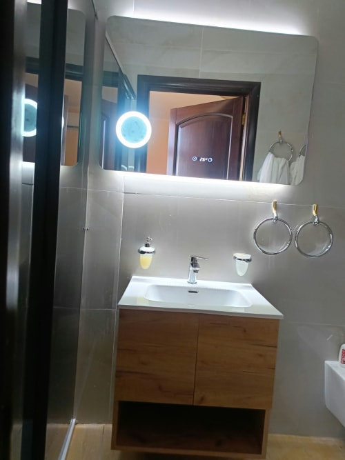 Bagno moderno dell'hotel Atena Smartrooms a Sellia con specchio illuminato, lavabo bianco, mobile in legno e doccia in vetro
