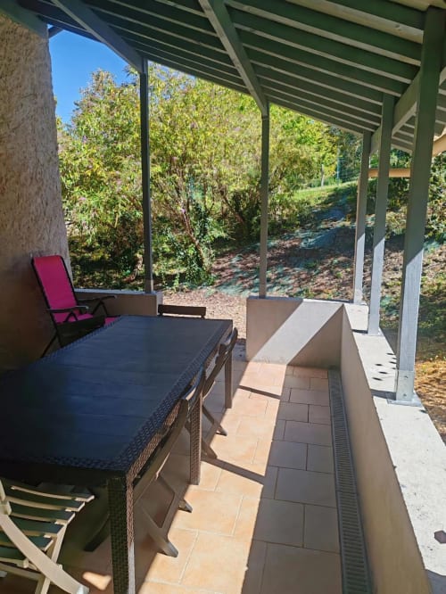 Terrasse couverte aux Gîtes De Petrocoriis avec vue sur le jardin, table de salle à manger et chaises longues