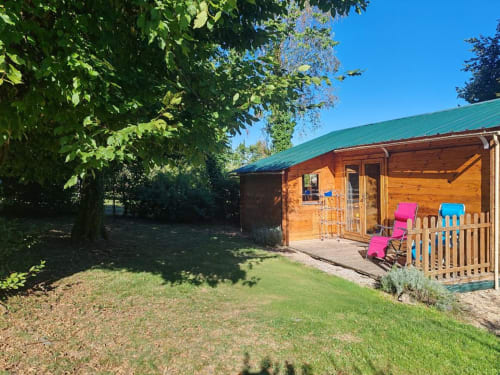 Gîte Le Verger aux Gîtes De Petrocoriis : chaumière bois, jardin, chaises roses sur véranda, toiture verte, Boulazac