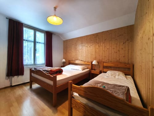 Chambre cosy pour 3 personnes au Chalet Coste Belle à Ceillac : murs en bois, deux lits, vue montagne et luminaires chaleureux