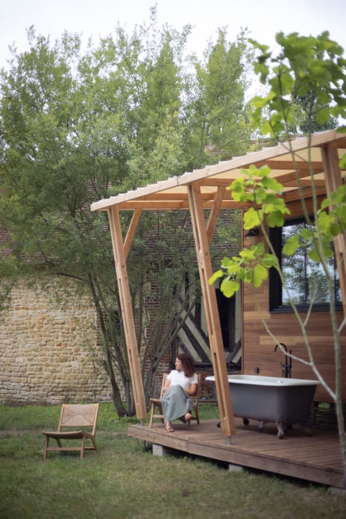 Vrouw ontspant onder een houten pergola op het terras met hottub, tuinzicht van villa Domaine de Blanvatel, Saint-Pierre-en-Auge