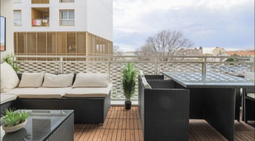 Terrasse moderne de Q&R Renting à Nice avec mobilier en rotin noir, terrasse en bois, plantes en pot et vue sur la ville