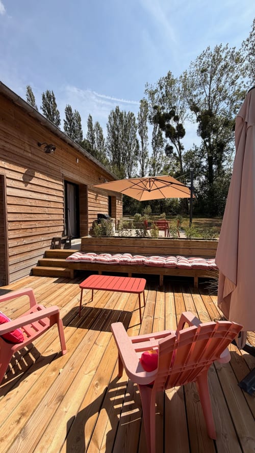 Houten terras van Domaine de Blanvatel met roze stoelen, oranje parasol en tuinuitzicht in Saint-Pierre-en-Auge
