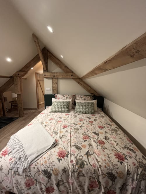 Rustieke zolderkamer met blootliggende houten balken, bloemenprint beddengoed en inbouwverlichting in Domaine de Blanvatel