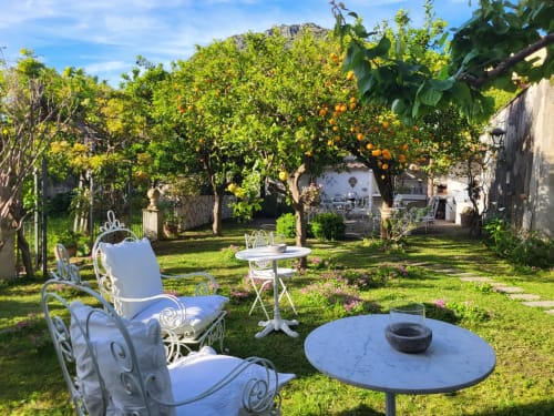 Suggestivo cortile del Relais Palazzo Cacace a Meta di Sorrento con sedute ornamentali bianche, agrumeti e zona fuoco