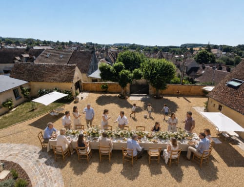 Vue aérienne d'une longue table de salle à manger dressée dans une cour de la Casa Pertica à Ceton, France, avec des invités se rassemblant pour