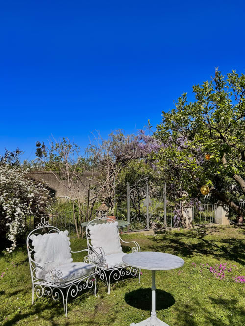 Eleganti sedie in ferro battuto bianco in lussureggiante giardino con piante fiorite al Relais Palazzo Cacace, Meta di Sorrento