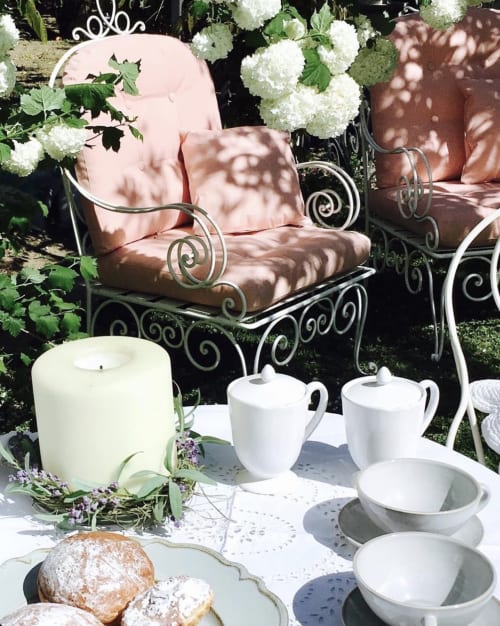 Area lounge del Relais Palazzo Cacace con sedia in ferro battuto, ortensie bianche, servizio da tè e pasticcini a Meta di