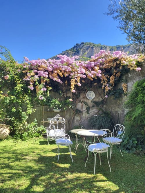 Incantevole area lounge nel giardino di Relais Palazzo Cacace a Meta di Sorrento con arredamento in ferro battuto e fiori rosa in fiore