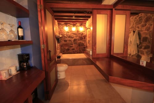 Baño de la habitación Magnolia en Casa Acento, Valle de Bravo, con muros de piedra, bañera de inmersión e iluminación cálida