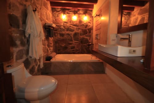 Baño de lujo en hotel Casa Acento, Valle de Bravo, con muros de piedra, bañera hundida e iluminación ambiental