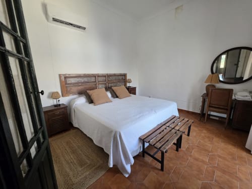 Amplia habitación en Hacienda Las Lumbreras en Montellano con cama de madera, ropa de cama blanca, pisos de terracota y estilo tradicional