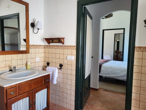 Baño de la Hacienda Las Lumbreras con tocador de madera, azulejos en el respaldo y vista hacia la habitación a través de puerta con marco verde