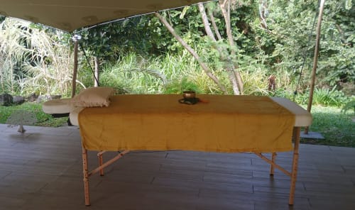 Table de massage au tissu doré sur terrasse bois, abritée par pergola avec vue sur jardin tropical au Domaine de Jade