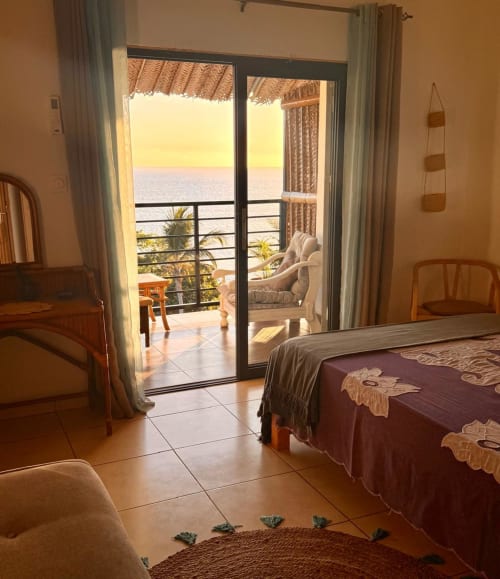 Chambre d'hôtel Le Chissioua avec balcon vue mer surplombant les palmiers et la côte méditerranéenne au coucher de soleil à Sada