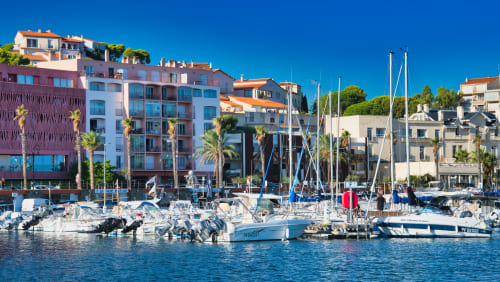 La Résidence du Fontaule, ses appartements sur le port de Banyuls-sur-Mer avec ses voiliers, en bord de mer et son architecture méditerranéenne sous un ciel bleu.