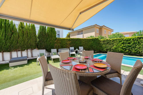 Alcudia villa ACACIAS outdoor dining area with wicker chairs, red place settings, private pool, yellow awning, and manicured