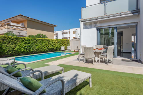 Modern villa in Alcudia with private pool, furnished terrace, lounge chairs, and manicured garden under clear sky