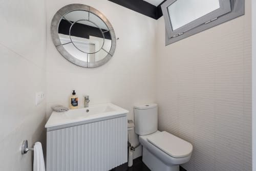 Modern bathroom in MallorcaWeek villa, Alcudia with white sink, toilet, circular mirror and skylight window