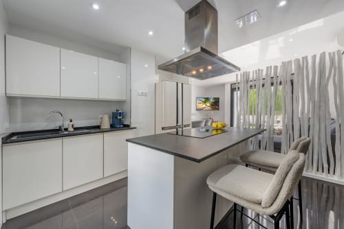 Modern villa kitchen in Alcudia with white cabinetry, dark countertop island, stainless steel range hood, and bar seating