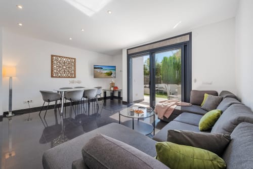 Modern villa living area in Alcudia with gray sofa, dining table, and terrace access overlooking garden