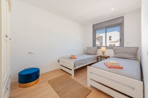 Bright twin bedroom in Alcudia villa with white beds, blue ottoman, wooden floor, and terrace view
