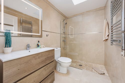 Modern bathroom in Alcudia villa with beige tiles, wooden vanity, glass shower enclosure, and heated towel rails