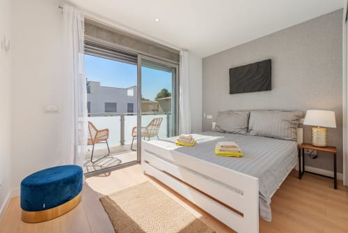 Modern bedroom in Alcudia villa with terrace view, queen bed, TV, nightstand lamp, and access to private outdoor seating area